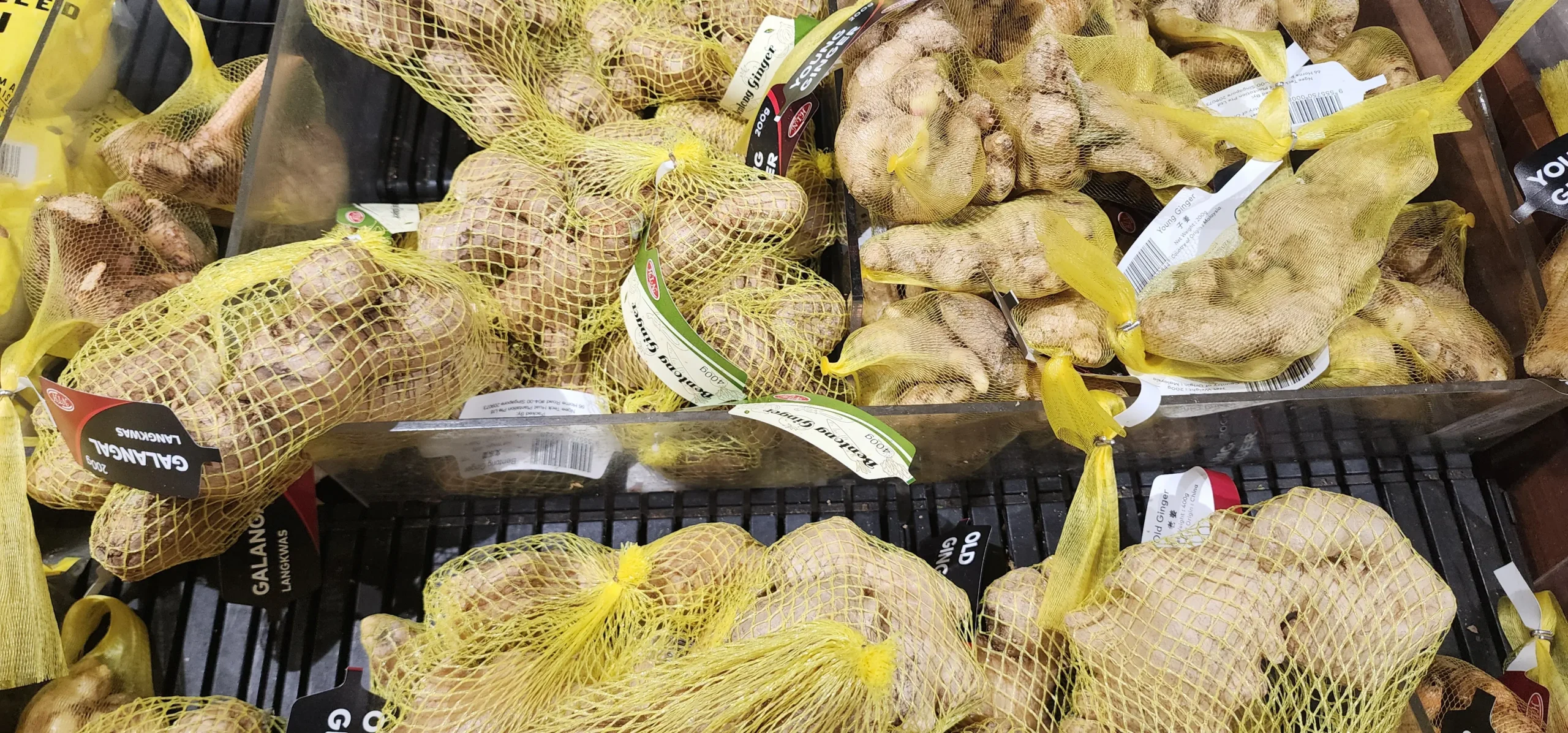 Fresh ginger roots displayed in mesh bags at a supermarket produce section
