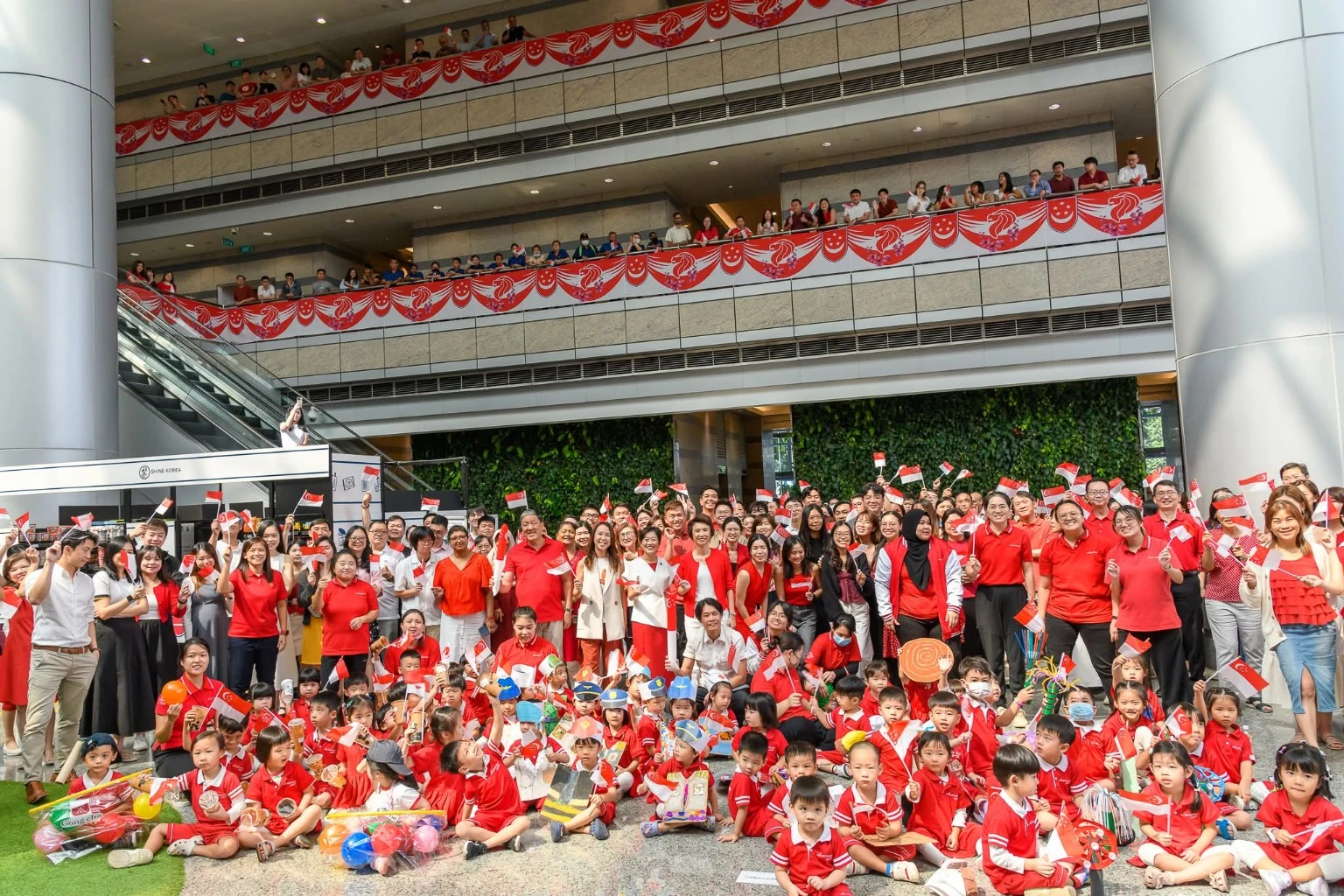 Children and adults gathered with Singapore flags at a school community event in The JTC Summit atrium.