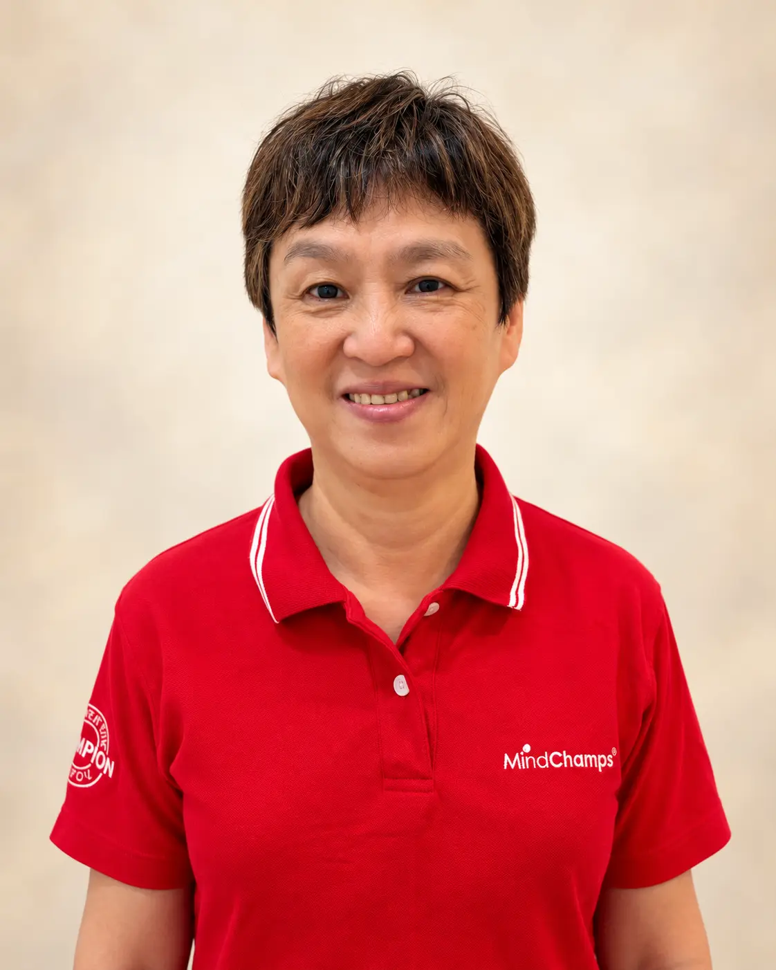 Portrait of Principal Christina Tan in her red MindChamps polo shirt, with a digitally refined ivory background.