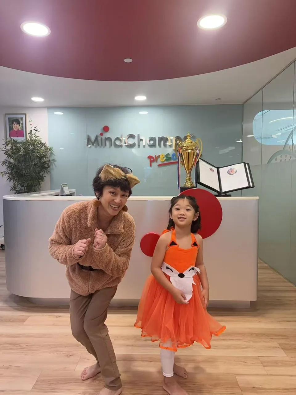 Ms Chris posing playfully beside a child in an orange fox costume.
